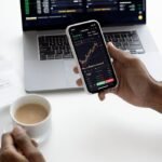 Person analyzing stock market trends on smartphone with laptop background
